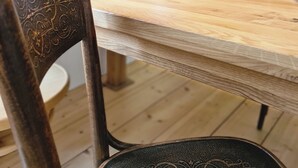 A wooden dining table with a white vase of flowers, a wine glass, and a chair with a decorative backrest. - Adorable 2-bedroom apartment  - TGM 2 (Český Krumlov)