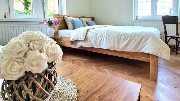 A bedroom with a bed, a wooden headboard, a window, and a wicker basket with white flowers. - Adorable 2-bedroom apartment  - TGM 2 (Český Krumlov)