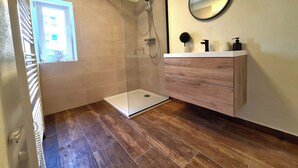 A modern bathroom with a glass-enclosed shower, a wooden floor, a white vanity with a mirror, and a window providing natural light. - Adorable 2-bedroom apartment  - TGM 2 (Český Krumlov)