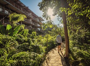 A pathway surrounded by lush greenery and a multi-story building with balconies. - Stunning 2BR Jungle Oasis Tulum | Gym | Coworking (Tulum)