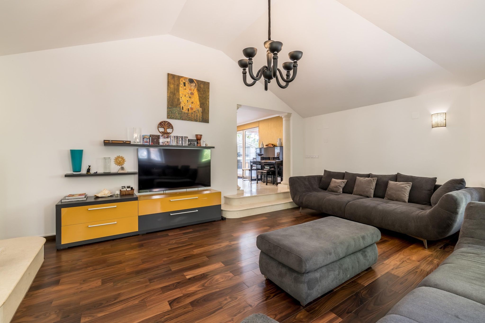Una sala de estar moderna con un televisor de pantalla plana, un sofá, un reposapiés y un comedor visible a través de una puerta abierta.