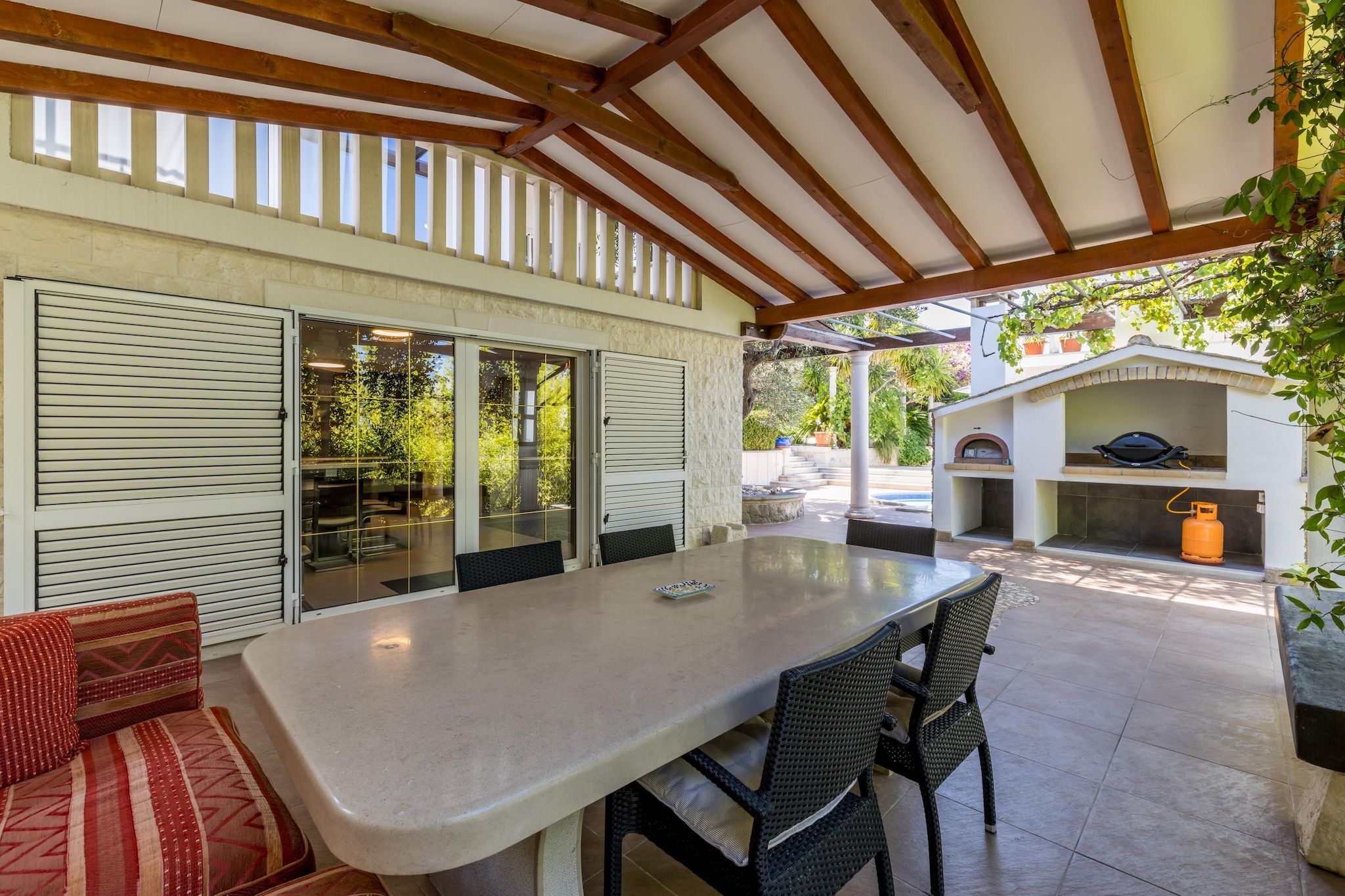 Un patio exterior con mesa y sillas, un área de estar cubierta y una parrilla.