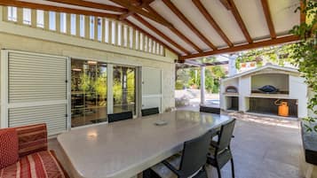 Un patio exterior con mesa y sillas, un área de estar cubierta y una parrilla.