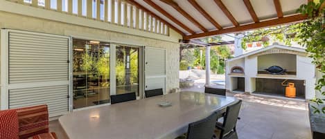 An outdoor patio with a table and chairs, a covered seating area, and a barbecue grill.