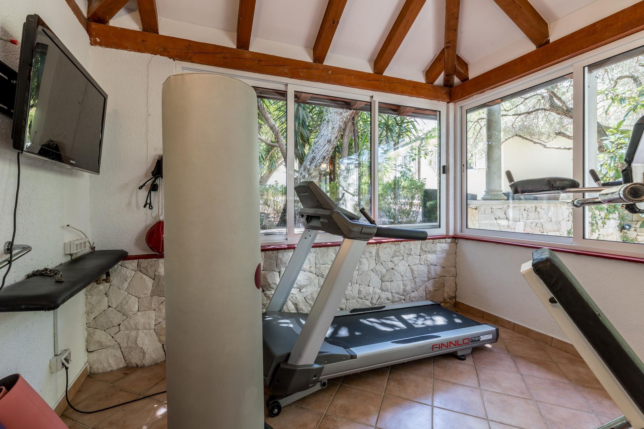 Un gimnasio en casa con una cinta de correr, equipo de ejercicio y un televisor montado en la pared.