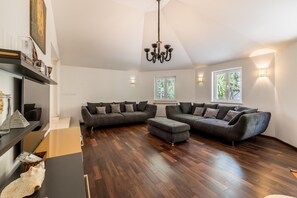 A spacious living room with a sectional sofa, a chandelier, and a view of the outdoors through large windows. - Luxury Garden Villa 50m from the Beach (Sutivan)