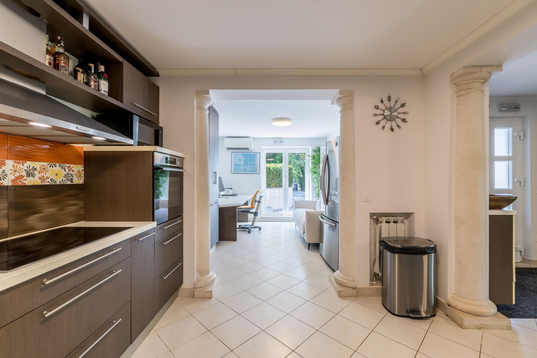 A modern kitchen with a central island, a dining area with a chair, and a trash bin.