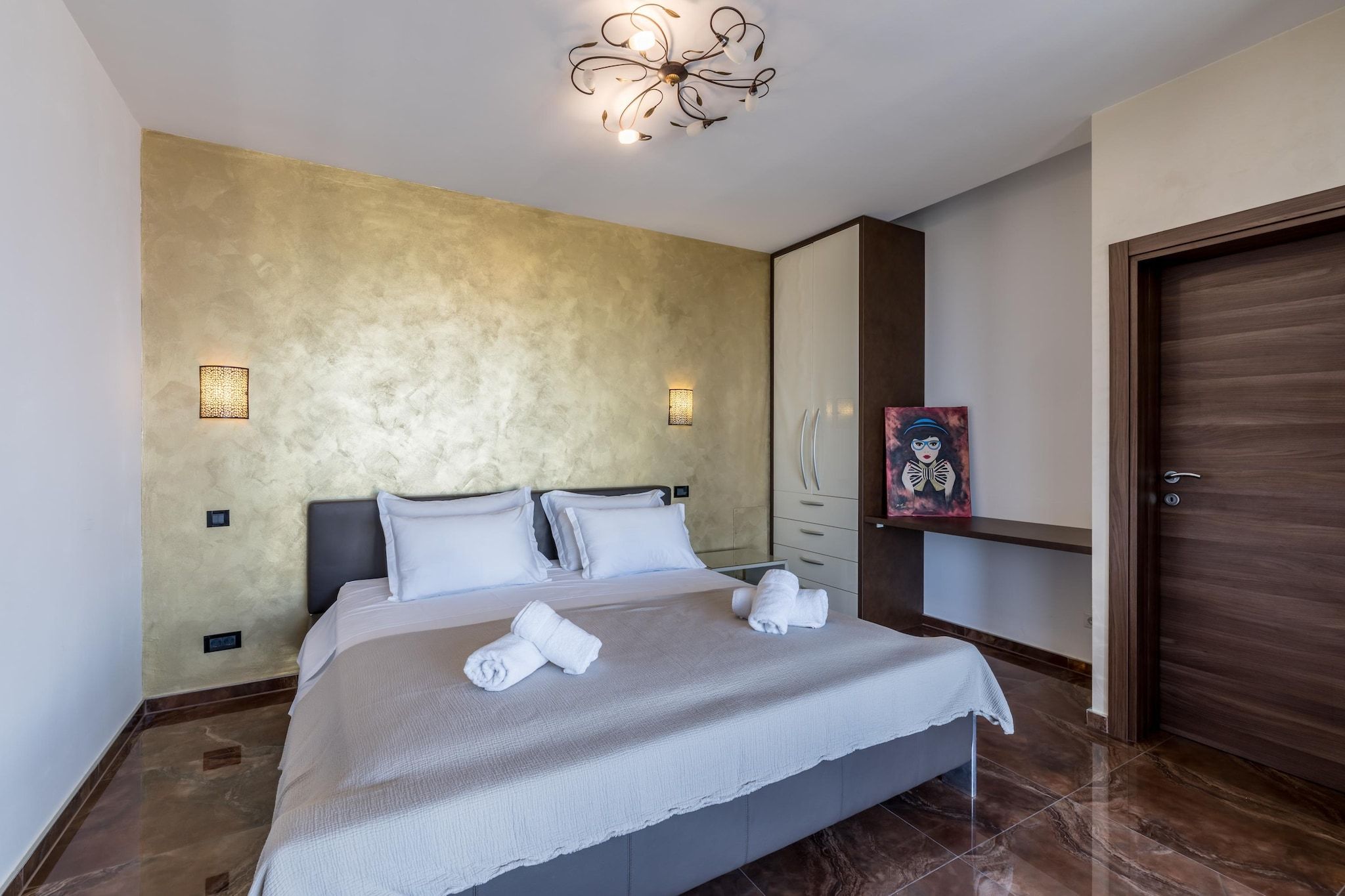 Una habitación de hotel con una cama, una lámpara de pared, una puerta y un cuadro en la pared.