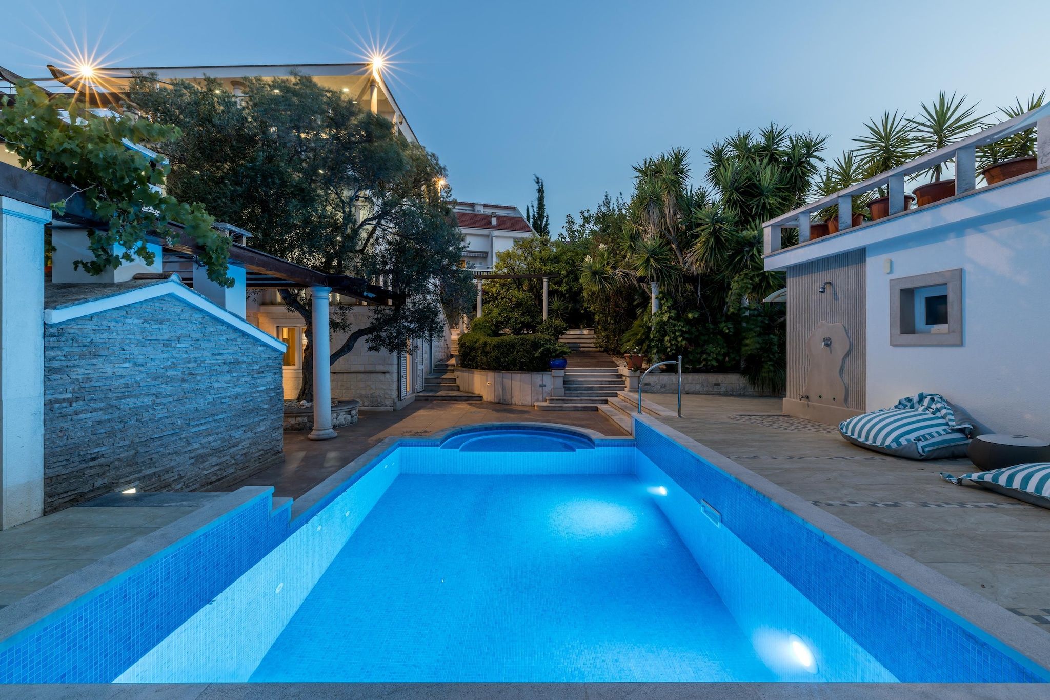 A swimming pool with a stone wall on one side and a white building with a red roof in the background.