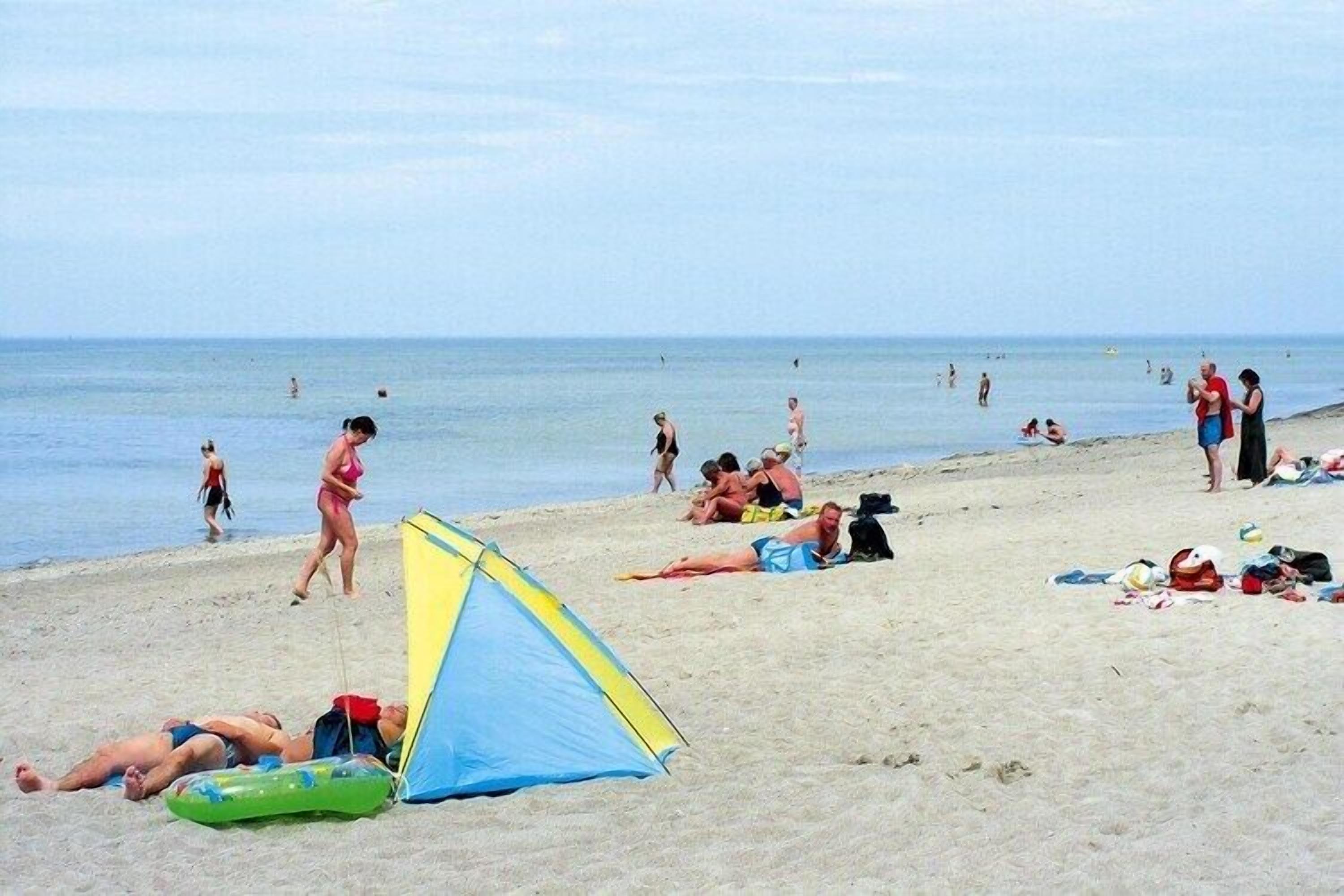 A beach with people sunbathing, a tent, and a person walking.