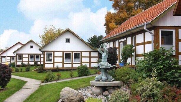 Un edificio de estilo europeo tradicional con un jardín que cuenta con una fuente de piedra y abundante vegetación.
