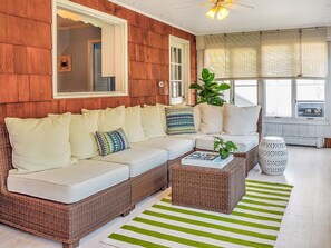 A cozy living room with a wicker sofa, a striped rug, and a large window with blinds. - Charming 5-bedroom house, block and a half to the beach in Bay Head (Bay Head)