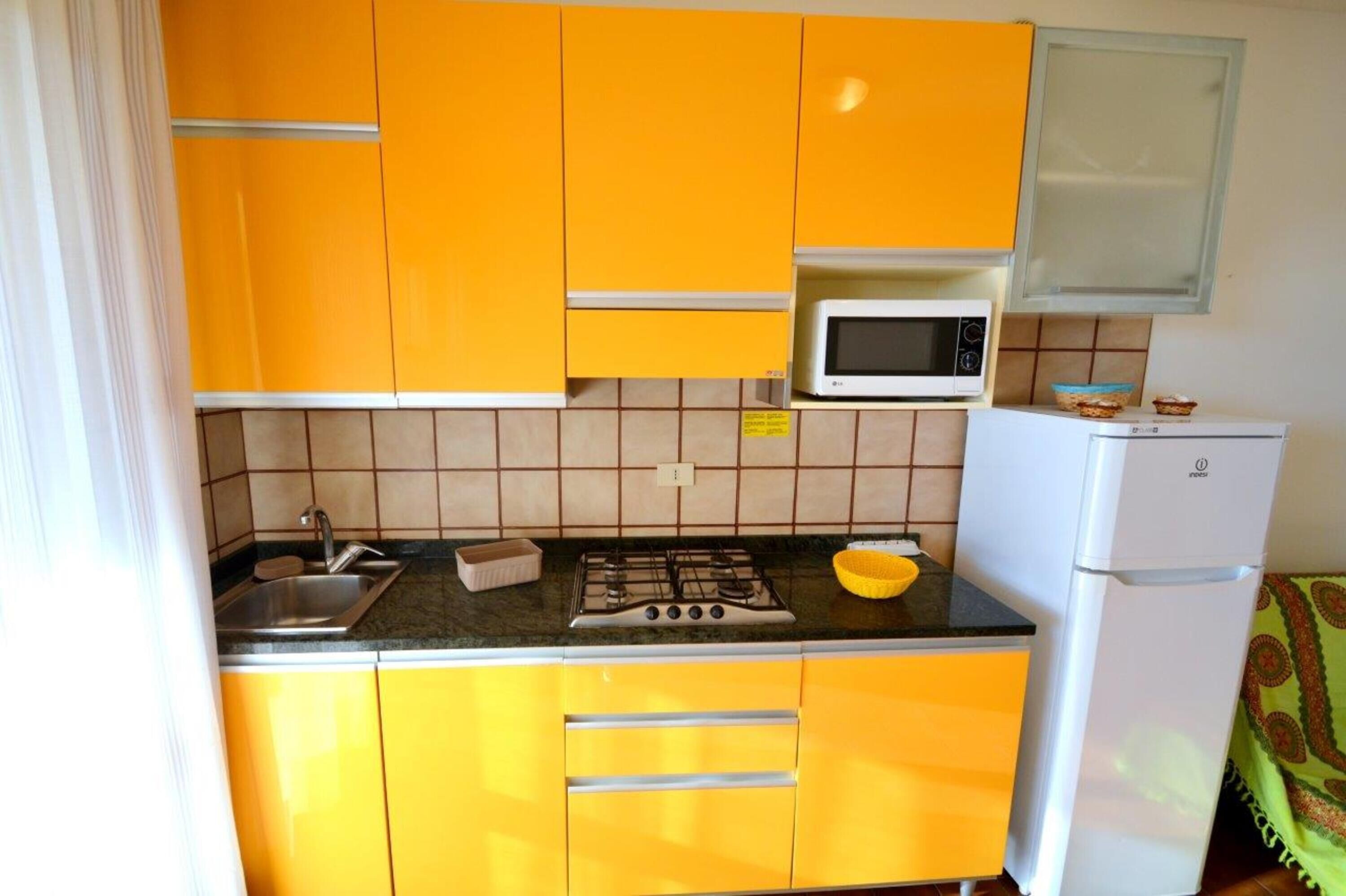 A compact kitchen with yellow cabinets, a gas stove, a microwave, and a refrigerator.