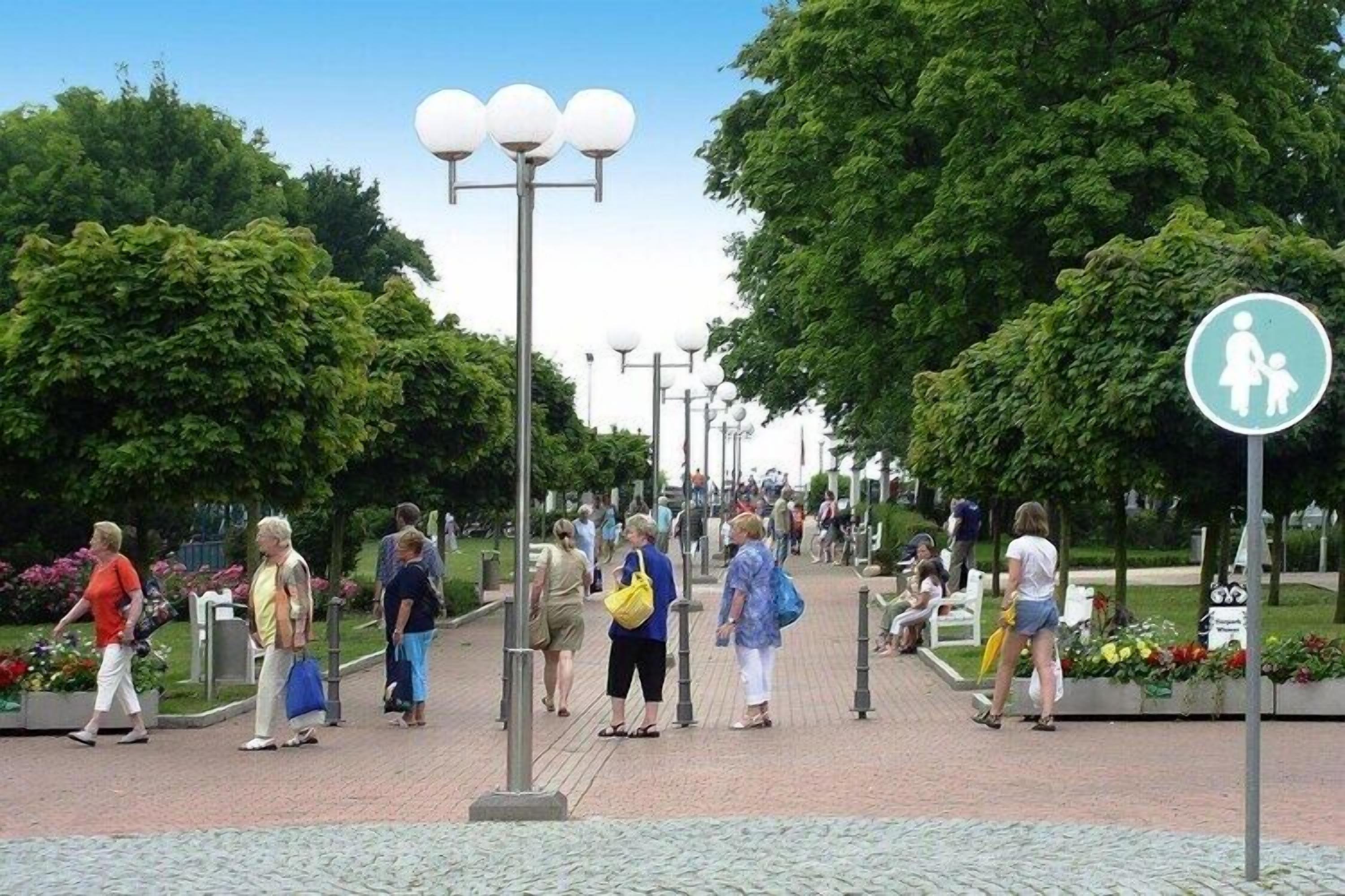 Un sendero peatonal con gente caminando, un cartel que indica zona familiar y farolas.