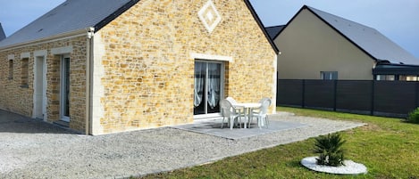 Un edificio de piedra con techo inclinado, una puerta y un pequeño patio con sillas.