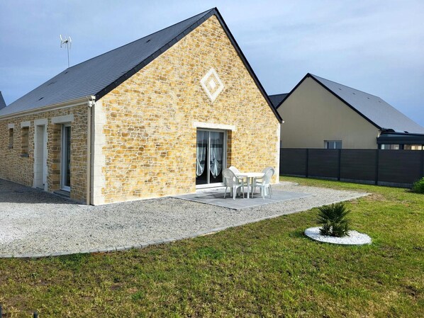 A stone building with a sloped roof, a door, and a small patio with chairs.