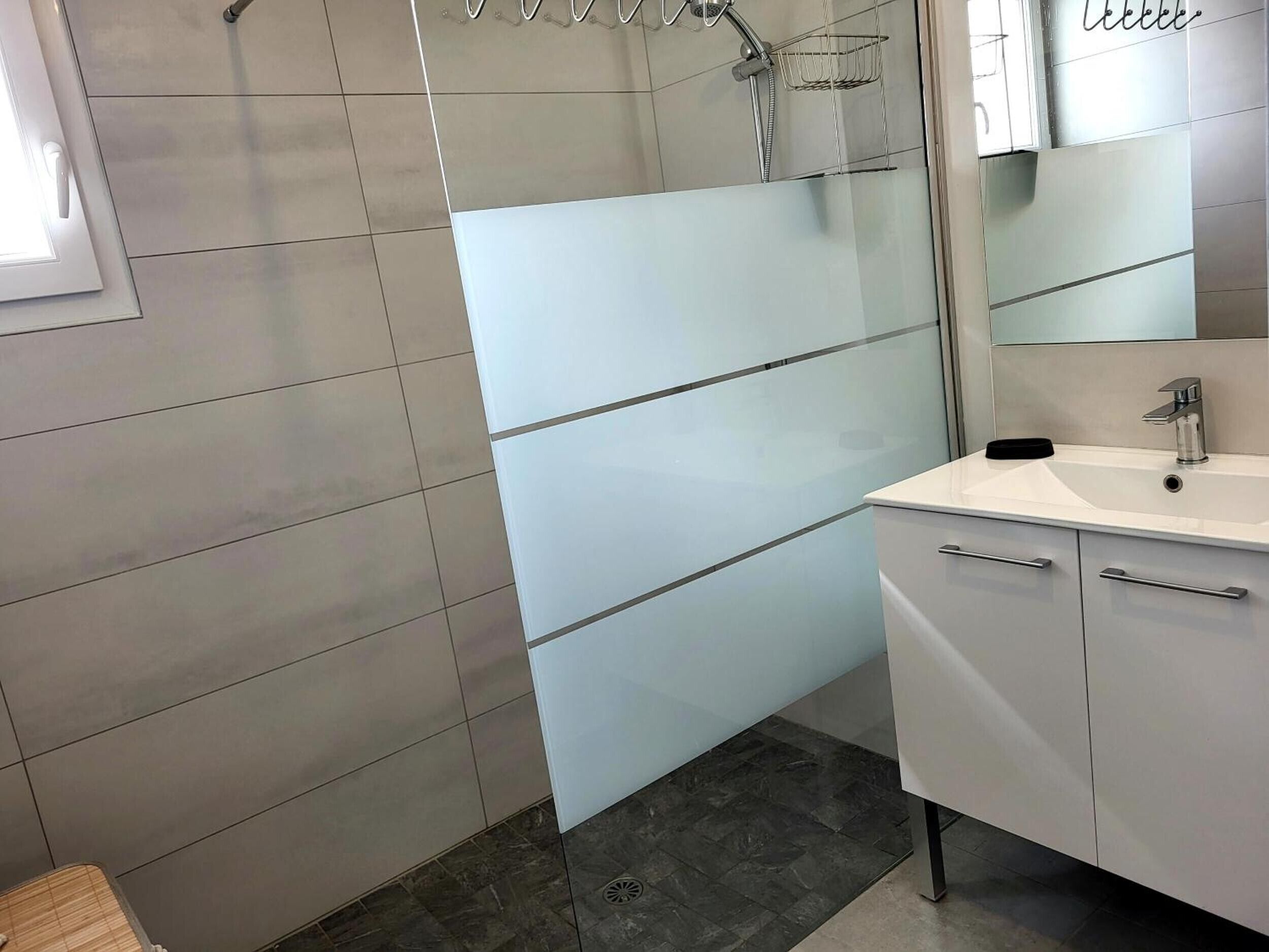 A modern bathroom with a white sink, mirror, and dark tiled floor.