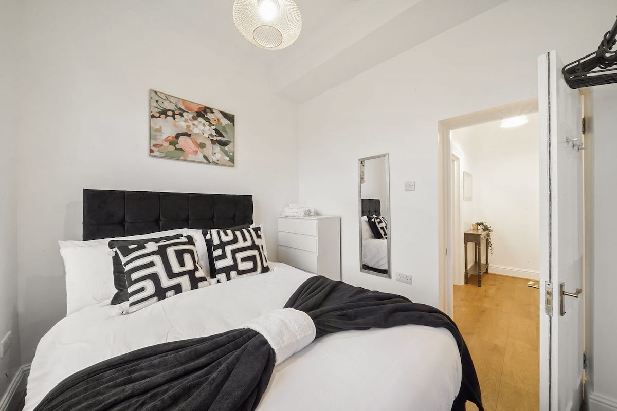 Un dormitorio con cama, mesita de noche, espejo y puerta que da a otra habitación.