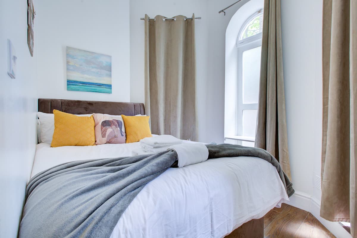 Un dormitorio con cama, cortinas, una ventana y un cuadro en la pared.