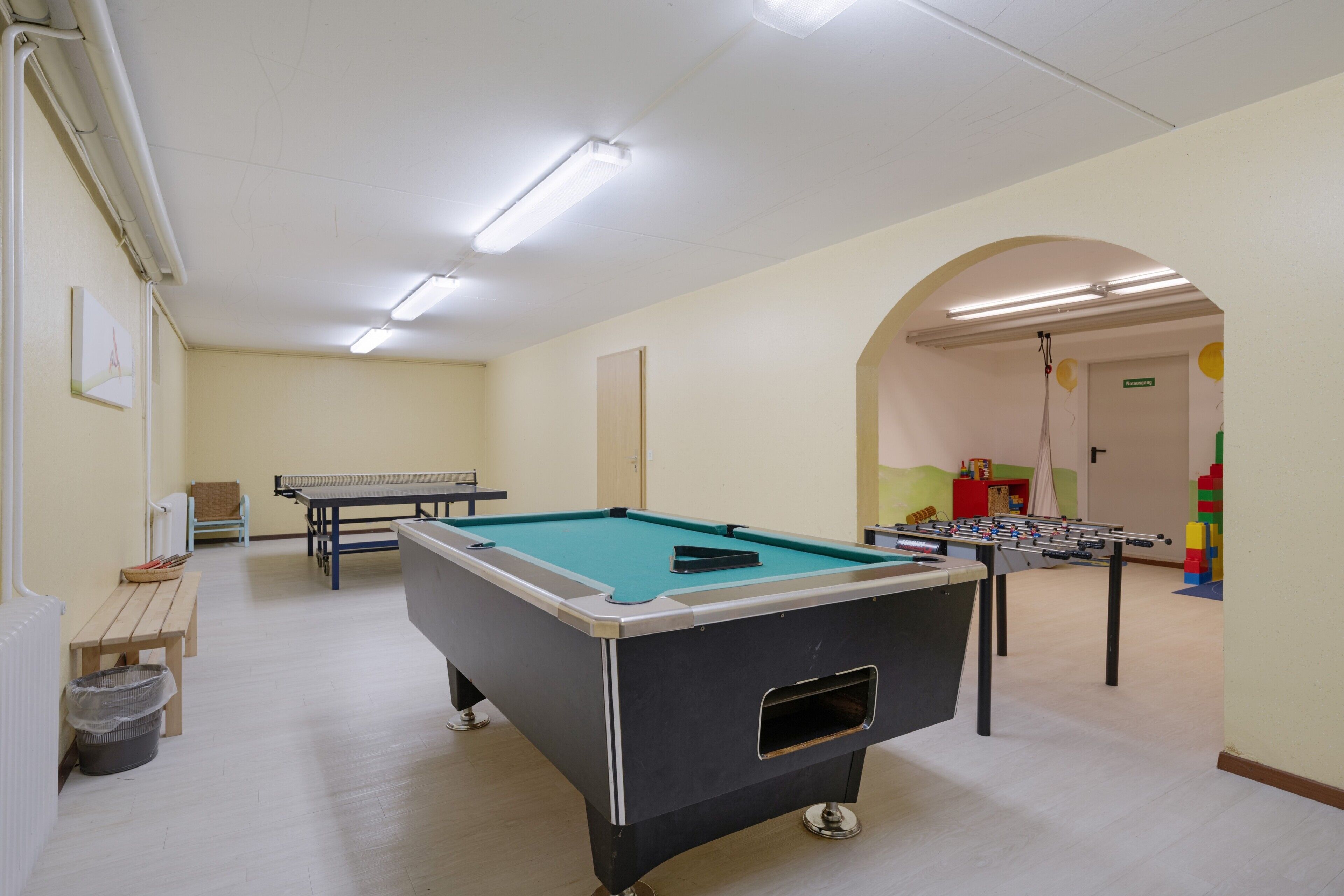 Una habitación con mesa de billar, mesa de futbolín y mesa de ping pong.