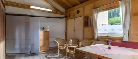 A wooden interior with a table, chairs, and a window with curtains.