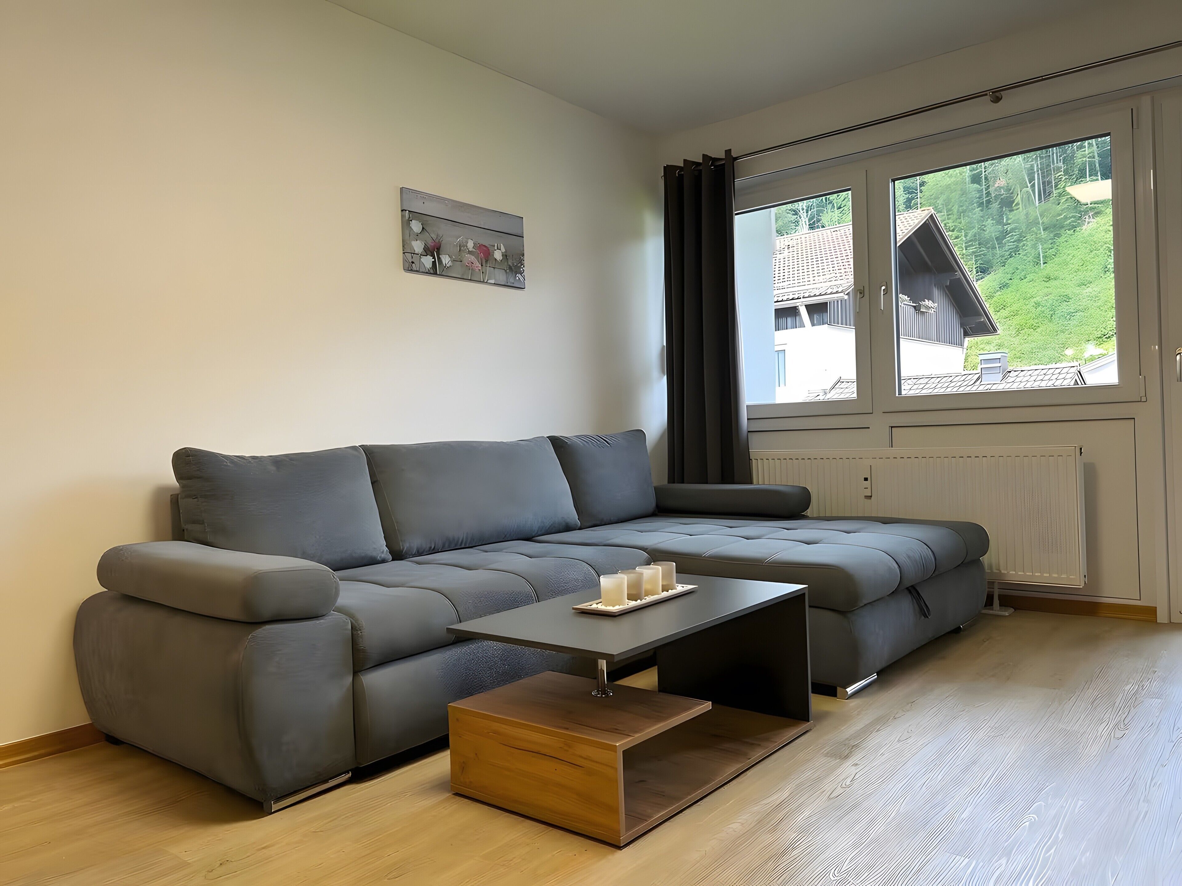 Una sala de estar moderna con un sofá seccional gris, una mesa de centro de madera y vistas a un edificio a través de una ventana.
