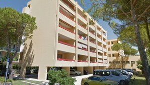 A multi-story building with a parking garage, trees, and parked cars. - Sweet Holiday Hideaway Near Bibione Beach (San Michele al Tagliamento)