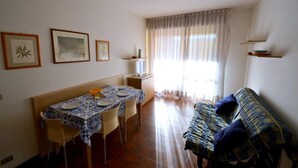 A dining area with a table set for four, a sofa, and a window with curtains. - Sweet Holiday Hideaway Near Bibione Beach (San Michele al Tagliamento)
