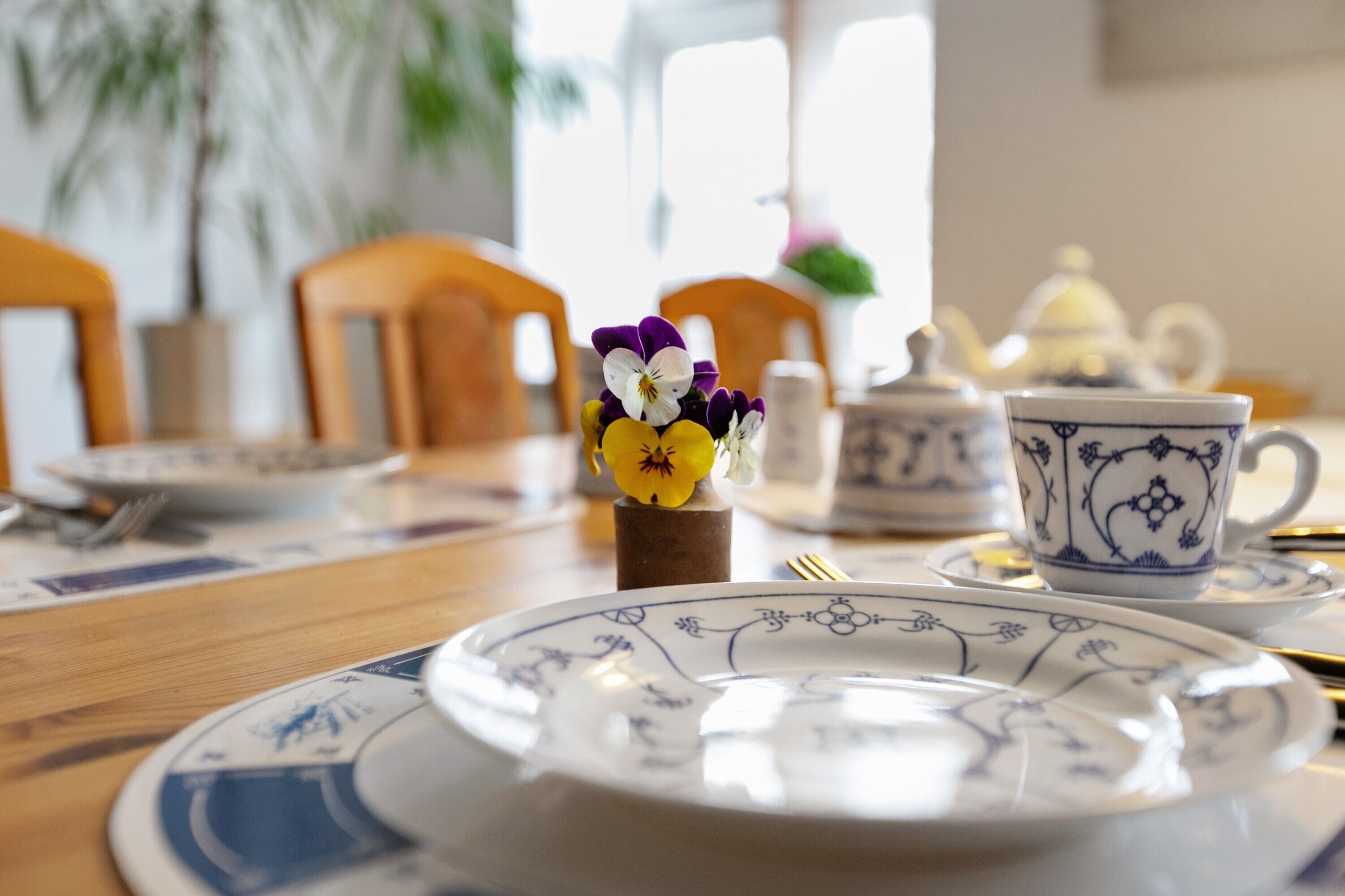 Uma mesa de jantar com pratos, um bule e um pequeno vaso com flores.