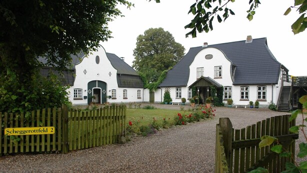 Een traditioneel wit gebouw met een grindpad en een houten poort.