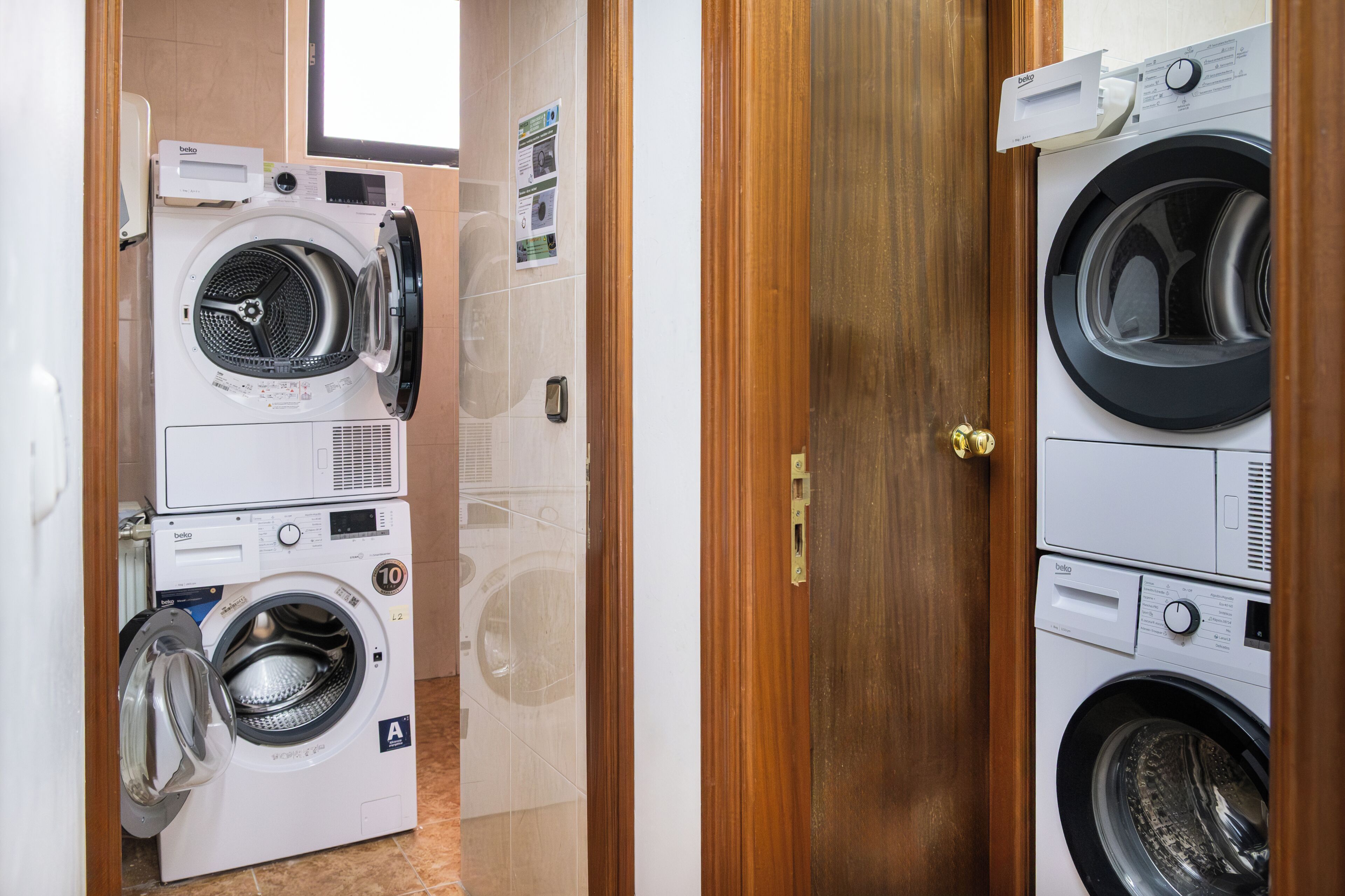 Un lavadero con lavadoras apiladas, una puerta de madera y un suelo de baldosas.