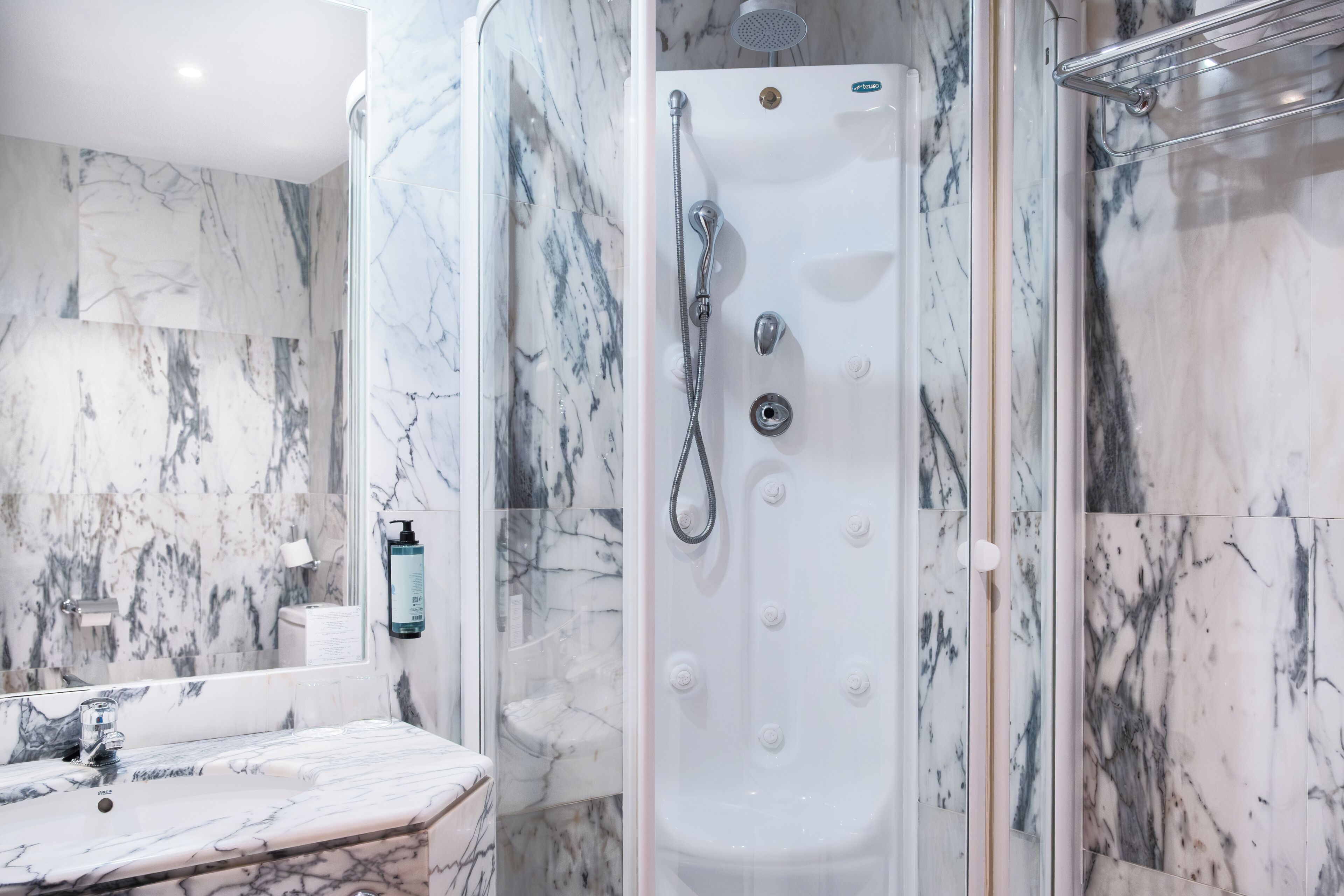 A modern bathroom with a marble shower, a sink, and a mirror.
