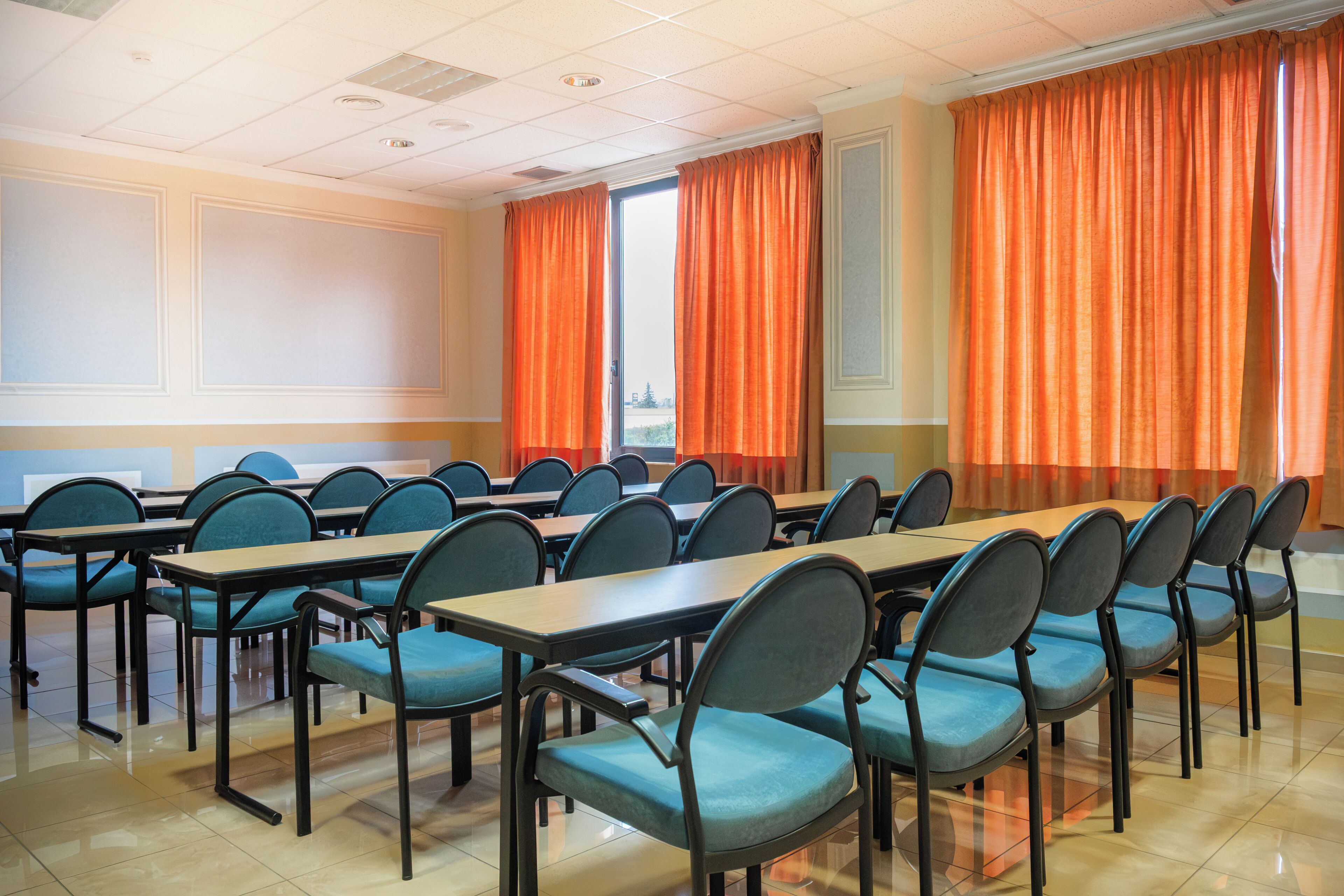 Un salón de conferencias con varias mesas y sillas, un ventanal con cortinas y vistas al exterior.