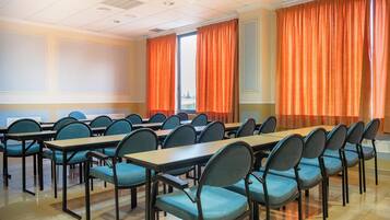 Un salón de conferencias con varias mesas y sillas, un ventanal con cortinas y vistas al exterior.