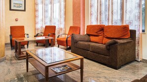 Eine Lobby mit einem braunen Sofa, orangefarbenen Sesseln, einem Glastisch und gemusterten Vorhängen.