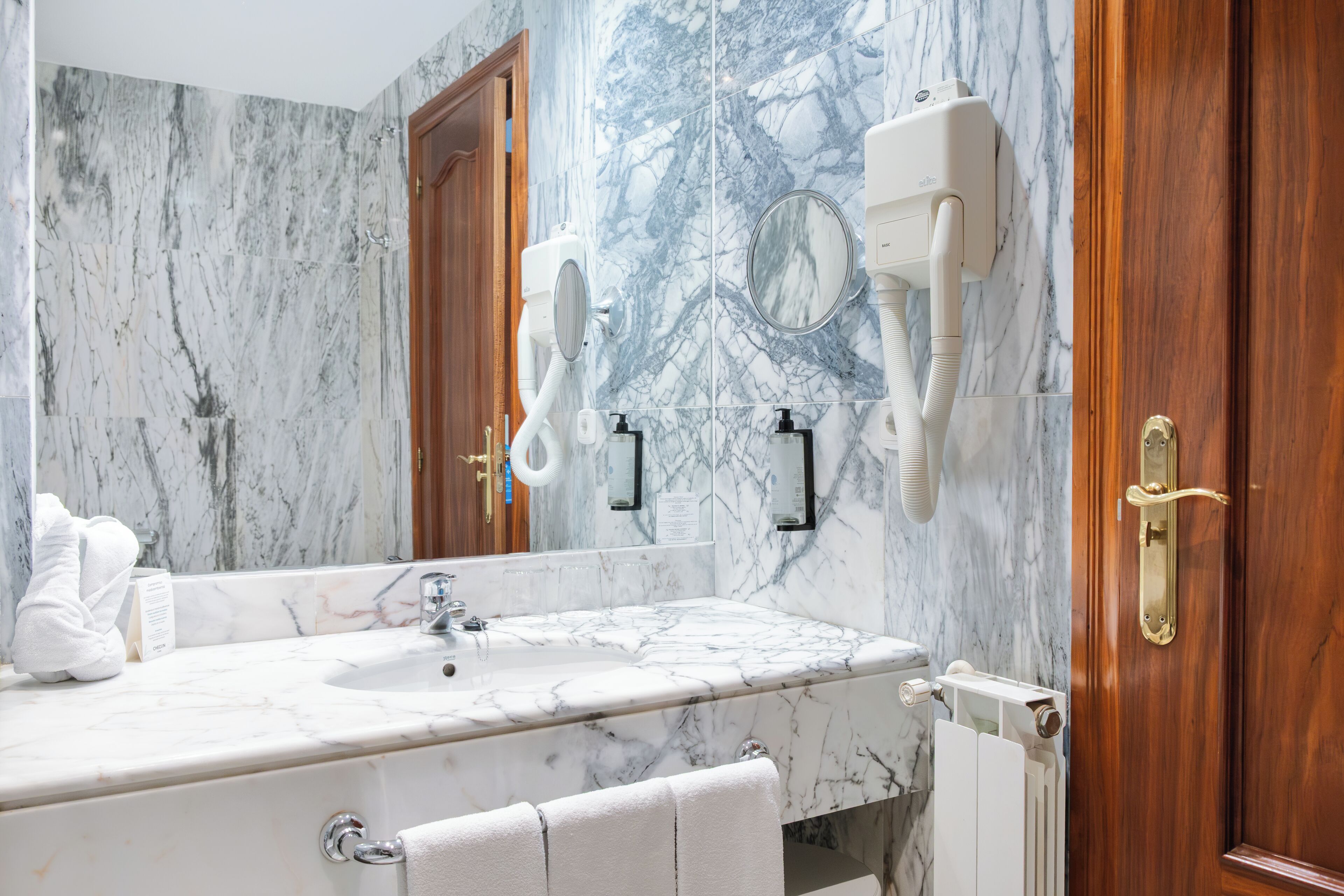A bathroom with a marble sink, a mirror, a hairdryer, and a towel rack.