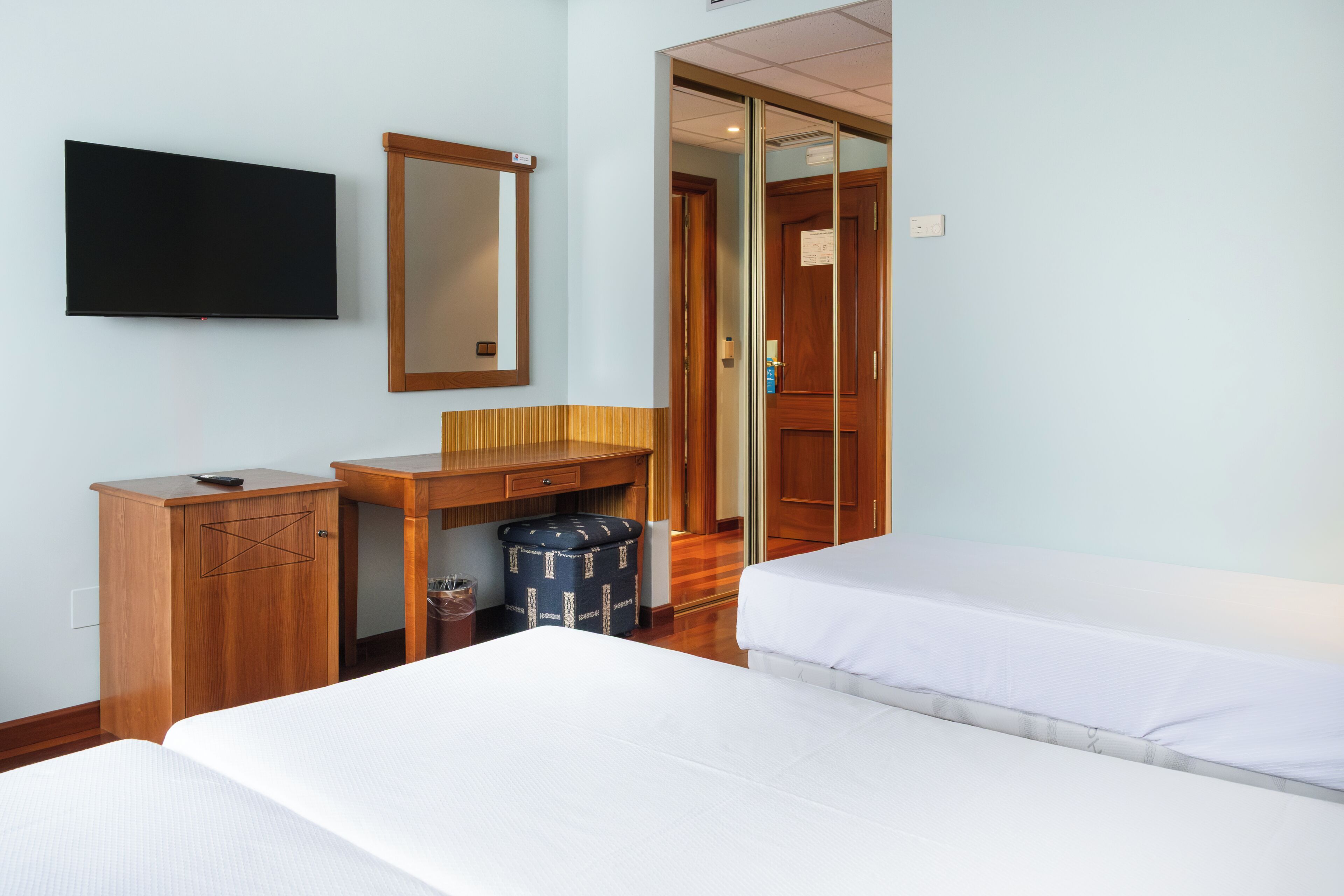 Una habitación de hotel con cama, escritorio, espejo y televisión.