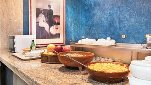 Ein Frühstücksbuffet mit Schüsseln voller Müsli und Früchten, einer Mikrowelle und einem gerahmten Bild an der Wand.