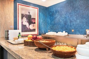 A breakfast buffet with bowls of cereal and fruits, a microwave, and a framed picture on the wall. - Checkin Basic León Norte (Villaquilambre)