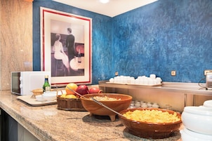 Un bufé de desayuno con tazones de cereales y frutas, un microondas y un cuadro en la pared.