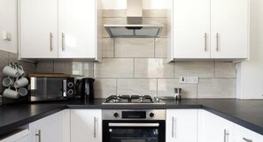 Eine moderne Küche mit weißen Schränken, einem Gasherd, einem Backofen und einer Mikrowelle.