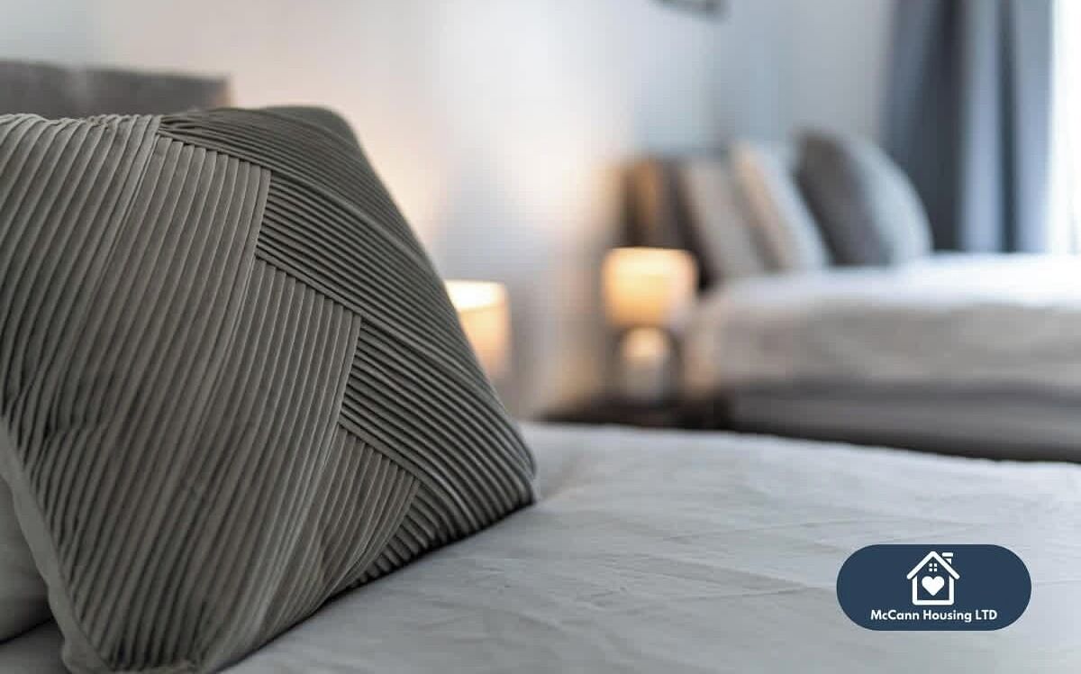 A hotel room with a neatly made bed, a pillow, and a lamp on the nightstand.