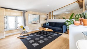 A living room with a blue sofa, a wooden coffee table, a rocking chair, a black rug, and a large mirror. - La Pomme des Chartrons – Apartment in Bordeaux, Wi-Fi & Air Conditioning (Bordeaux)