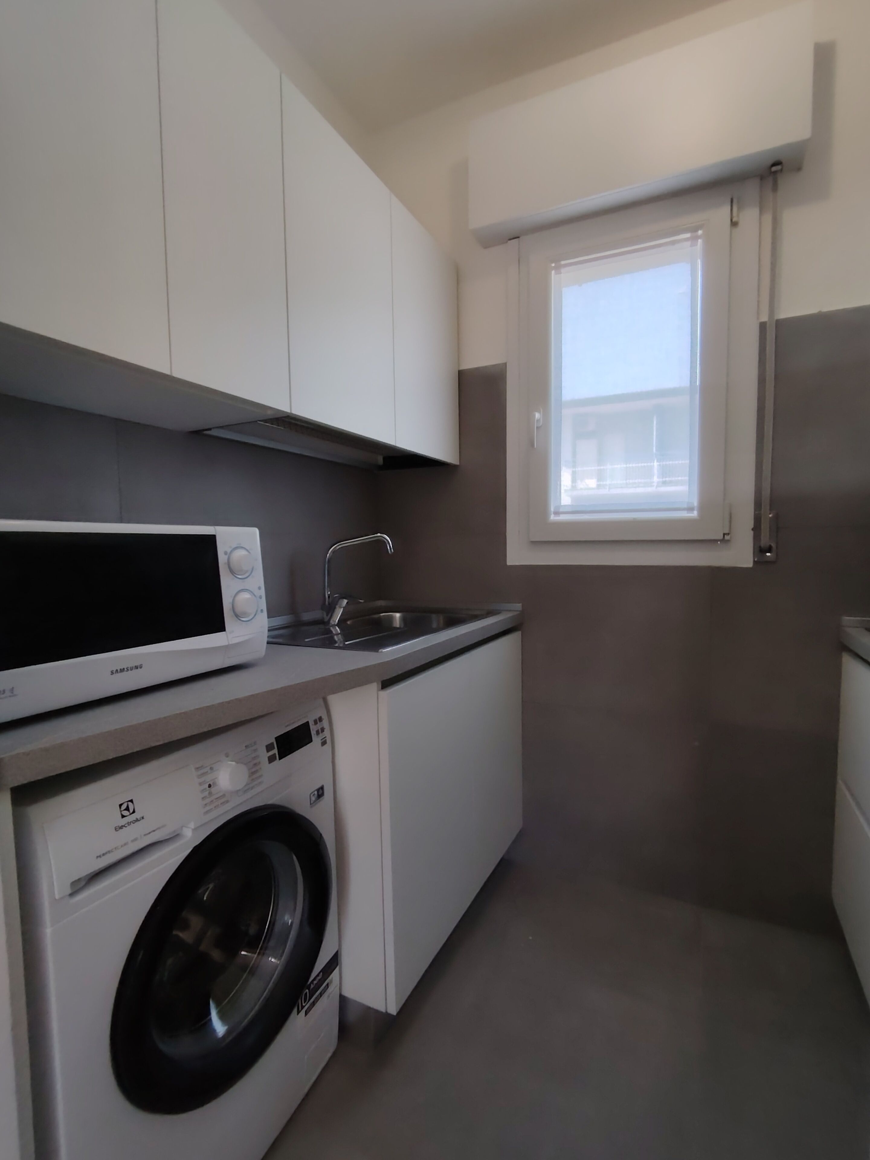 Een compacte keuken met een wasmachine, een magnetron en een raam met uitzicht.