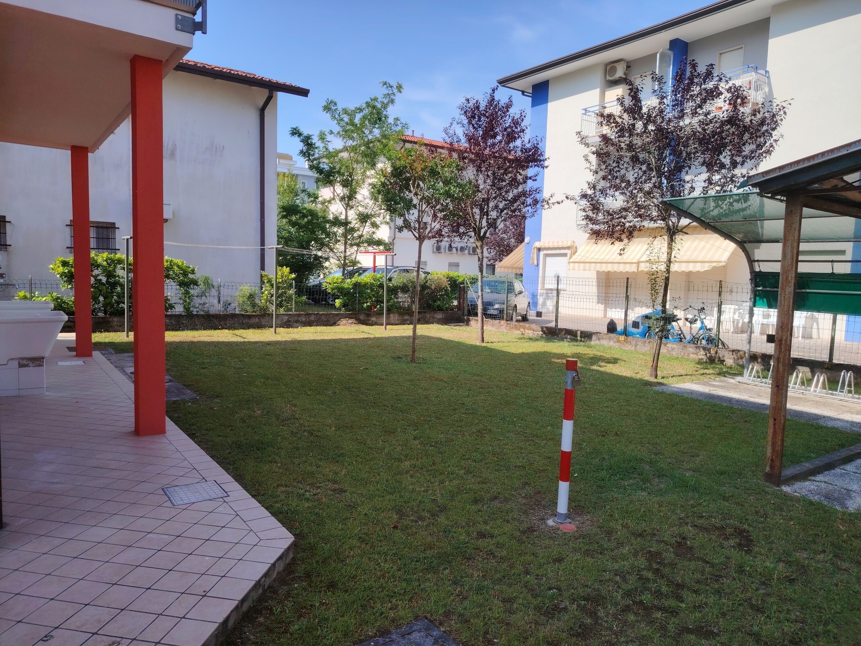 Un patio con suelo de baldosas, un bolardo rojo y blanco, y un edificio de fachada azul y blanca.