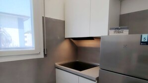 A compact kitchen with a built-in stove, a refrigerator, and a storage cabinet. - Stylish Flat for Your Perfect Getaway in Bibione (San Michele al Tagliamento)