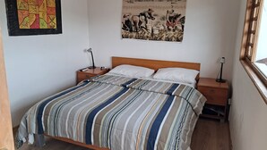 A bedroom with a wooden bed, two bedside tables, a nightstand, a tapestry, and a window with a view. - Your refuge in the Historic Center of Quito (Quito)