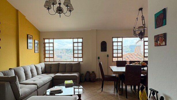 A living room with a sectional sofa, a dining table with chairs, a chandelier, and large windows with a city view. - Your refuge in the Historic Center of Quito (Quito)