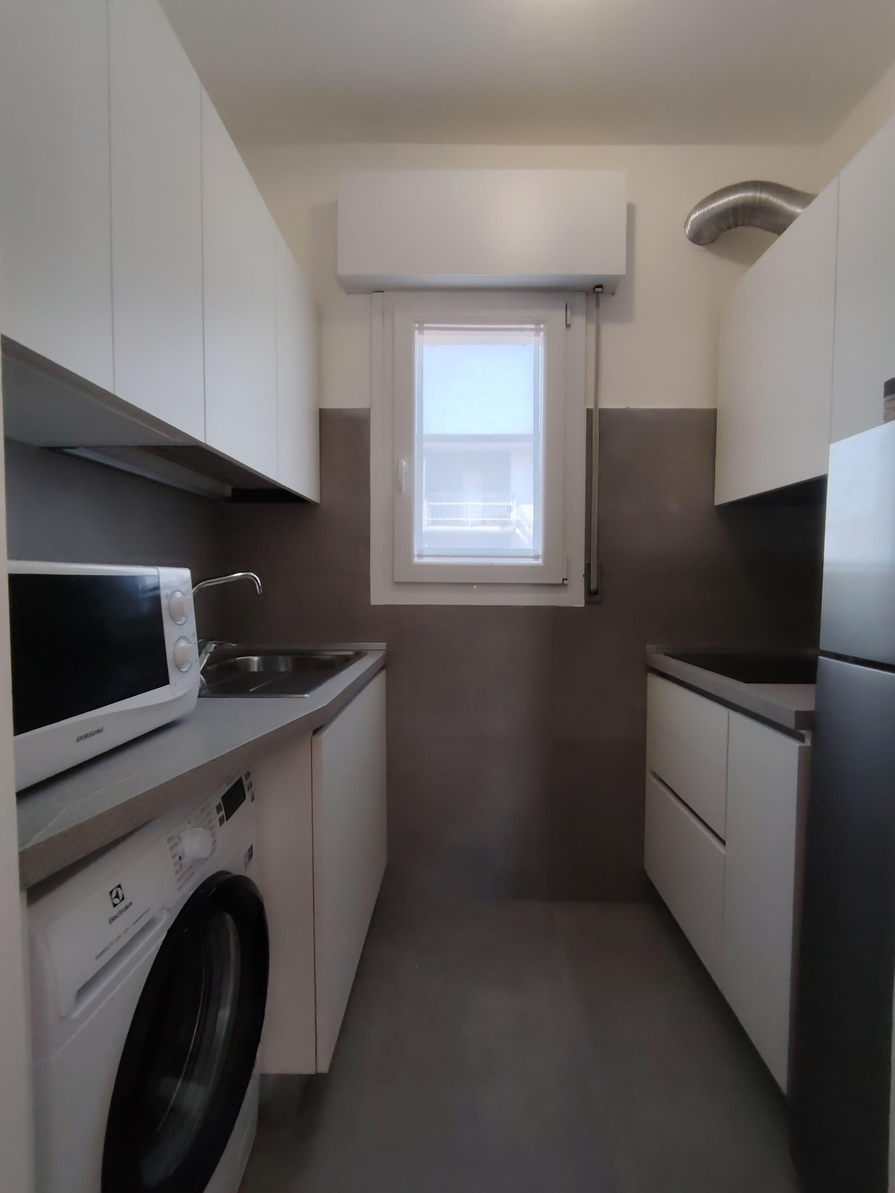 Cocina compacta con lavadora, microondas y una pequeña ventana.