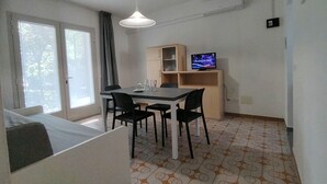 A small room with a bed, a table with chairs, a television, and a window with curtains. - Contemporary Flat Near the Beach of Bibione (San Michele al Tagliamento)